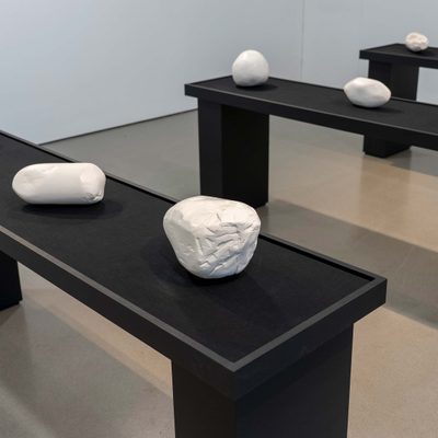 Three black benches hold roughly made, roundish white plaster sculptures.
