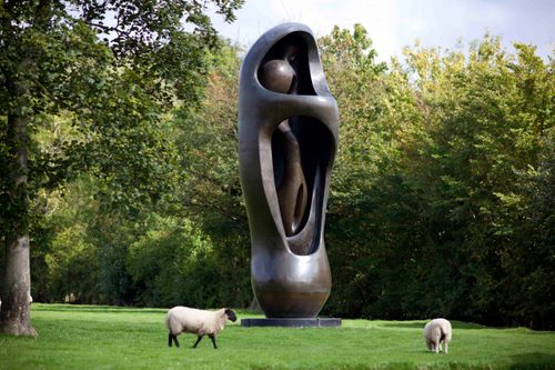 A huge bronze upright sculpture, standing in a green field surrounding by grazing sheep