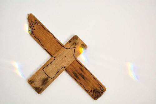 Two planks of wood, joined together in a cross, with the silhouette of a hawk-like bird drawn on top in black marker pen.