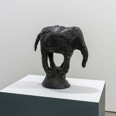 A dark, roughly textured sculpture of an abstract elephant with open spaces in its legs, which meet at the bottom to form a plinth.