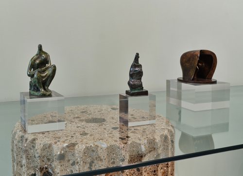 Three small bronze sculptures by artist Henry Moore, displayed on a glass table.