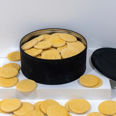 A black biscuit tin containing plaster digestive biscuits with braille text. More biscuits are on the table in front.