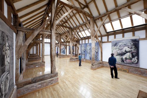 A wide shot of one wall in the Aisled Barn at Henry Moore Studios & Gardens, with visitors looking at four of Moore's tapestries hanging on the walls.