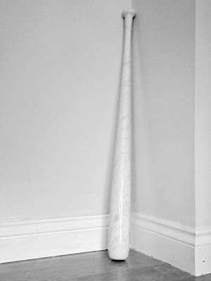 A white marble baseball bat, leaning against the corner of a white wall.