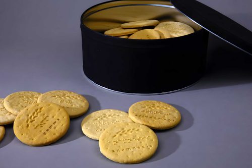 A black biscuit tin containing plaster digestive biscuits with braille text. More biscuits are on the table in front.