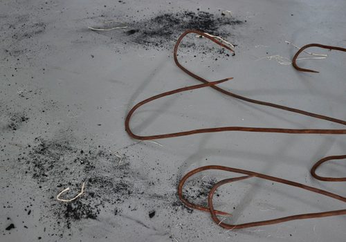 Close up view of part of a sculpture, showing the tips of several rusted iron hooks.