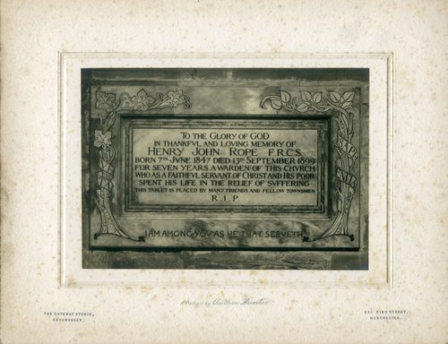 Black and white photo of the frontispiece for a tomb. It reads: 'To the glory of God, in thankful and loving memory of Henry John Rope FRCS. Born 7th June 1847 died 13th September 1899. For seven years a warden of this church, who as a faithful servant of Christ and his poor spent his life in the relief of suffering. This tablet is placed by many friends and fellow townsmen. R.I.P. I am among you as he that serveth.
