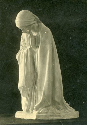 Black and white photo of a sculpture of a woman wearing a robe and shawl, who is kneeling in prayer.