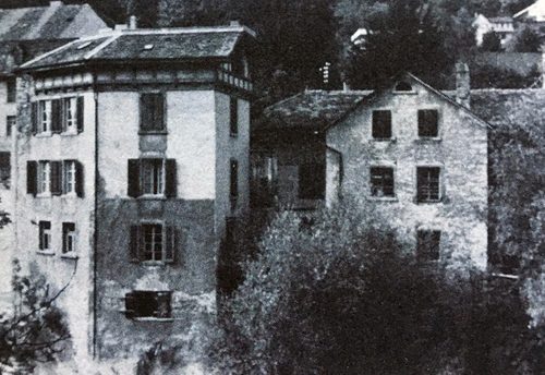 Black and white photo of a tall, narrow house with window shutters on a steep hillside