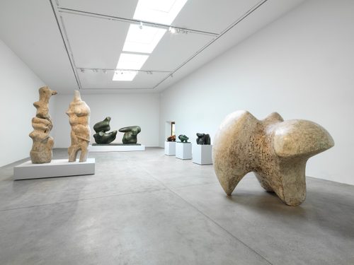 A white-walled gallery space with several large sculptures by Henry Moore. The largest, looking like the joint of a bone, is free-standing, with the others displayed on plinths.