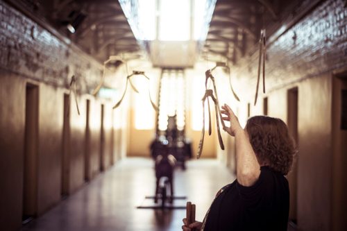 A woman is raising her hand to touch metal sculptures hanging from the ceiling. There are seven of them, each a vertical slice cut from a bell.
