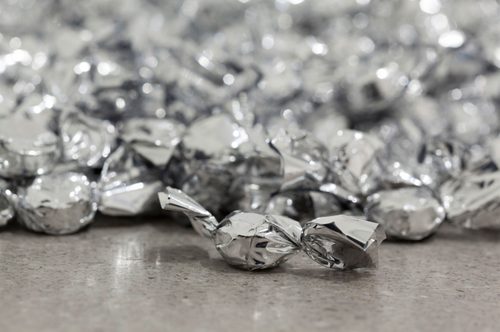 A close up photo of a pile of sweets wrapped in silver foil on a mottled grey floor.