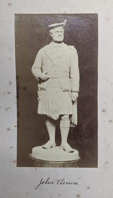 Black and white photo of a figurative sculpture of a man, formally dressed in a kilt and tom o' shanter (a type of flat cap).