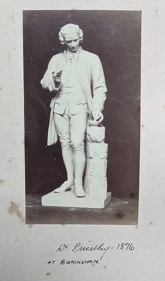 Black and white photo of a figurative sculpture of a man, who is mixing something with a mortar and pestle.