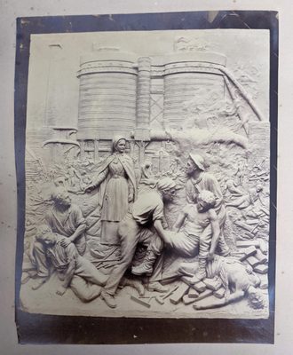Black and white photo of a relief sculpture of an industrial accident. A woman stands in the foreground next to several workers, who are lifting dead or injured bodies.