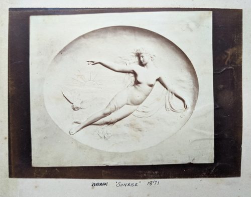 Black and white photo of a relief sculpture of a naked woman, floating in mid-air with an owl as the sun rises behind her.