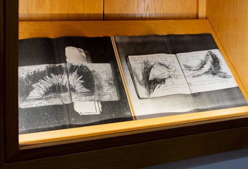 Display cabinet with two open books showing charcoal drawings.
