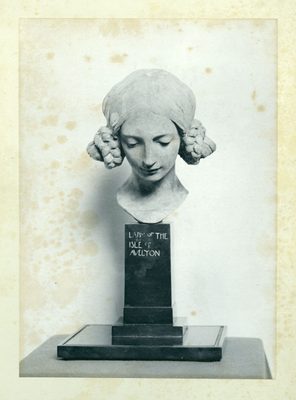 Black and white photo of a plaster portrait bust of a young woman. Her hair is in braids and she is looking down demurely. Text on the plinth reads 'Lady of the Isle of Avelyon'.