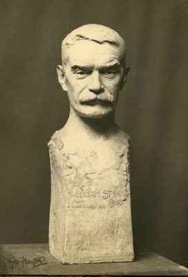 Black and white photo of a plaster portrait bust of a middle-aged man with short hair and a thick moustache. Text on the bust reads 'To William Strang, from Geo Frampton 1903'.