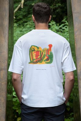 A white man with a freckled face and brown hair faces away from the camera. He is wearing a white t-shirt with an abstract design by Henry Moore of a reclining figure drawn in yellow, green and orange felt-tip pen. Behind the model is a bronze sculpture by Henry Moore.