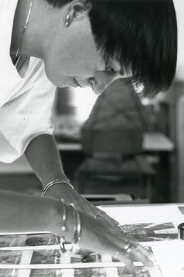Black and white photo of a woman at work arranging photographs.