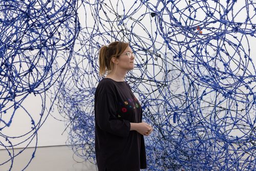 A woman walks through Lungiswa Gqunta’s sculpture 'Ntabamanzi', made from barbed wire and blue wool. The sculpture is designed to look like a wave breaking against the wall of the gallery.