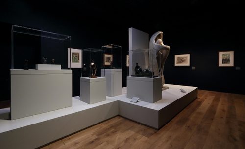 Gallery shot showing several sculptures by Henry Moore, displayed on plinths. There are framed drawings on the walls behind.