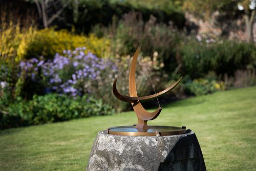 A small bronze sundial, sculpted by Henry Moore, in the garden at the artist's home. Behind the sundial is a border of lavender and cottage planting.