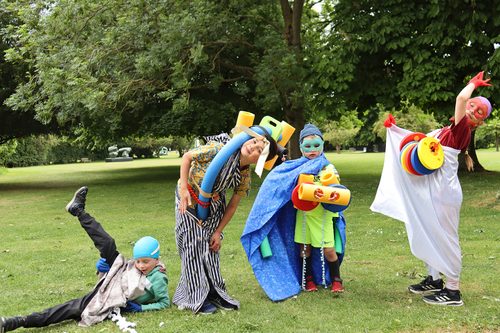 Four children wearing costumes made from brightly coloured fabrics and foam shapes. They are all posing pretending to be sculptures.