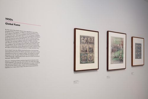A gallery with three framed drawings hung on the wall, variously depicting groups of people and reclining figures. A text display panel reads '1950s: Global Fame'.
