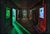 Drawing of a futuristic or alien room, featuring wall-mounted display screens showing images of human and alien faces. The walls and other surfaces look to be made of a dark metal, lit by neon greens and reds.