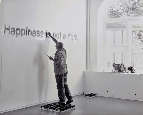 Black and white photo of a man painting a sign on a gallery wall, which reads 