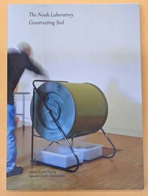 Cover of the book 'The Noah Laboratory: Constructing Soil' by John Newling. A man, blurred by motion, has an arm outstretched towards a sculpture comprised of a large, horizontal cylinder; it looks like he is spinning it.