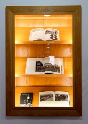 A display cabinet with four books. Three are opened at pages with black and white photos.