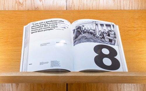 An open book, displaying a quote by Joseph Beuys, a black and white photo of the artist planting a tree, and a giant number 8.