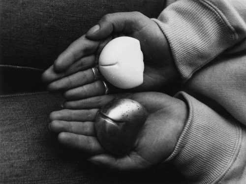 A pair of hands holding two simple sculptures, one black and one white. There are roughly palm-sized, round at one end and flat at the other, with a y-shaped line carved into the rounded end to make them look somewhat like bums.