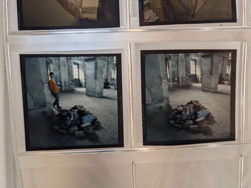A folder of small square photos of an exhibition by Julia Wood. In one, the artist casually leans against a wall next to her sculpture.