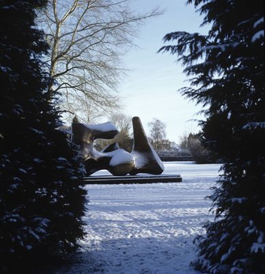 A huge bronze, abstract sculpture in a snowy field. The sculpture is also dusted with snow