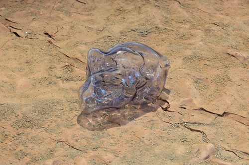 Detail of Lungiswa Gqunta's installation 'Zinodaka', showing an amophous, clear glass sculpture resting on a bed of dried, cracked clay.