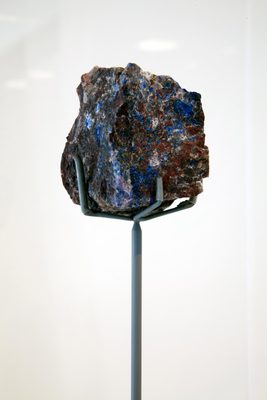 A black rock with streaks of bright blue, held up on a museum armature.