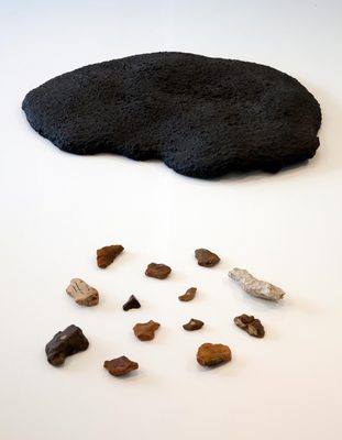 A round, flat lump of black asphalt, with a collection of small chipped stones in front.
