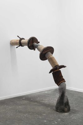 Abstract sculpture, tubular in form, bending from the floor to a wall somewhat like a pipe or a root. It is made in sections with different materials, including stone, iron, palm tree, wood salvaged from furniture, and miscellaneous pieces from abandoned factories.