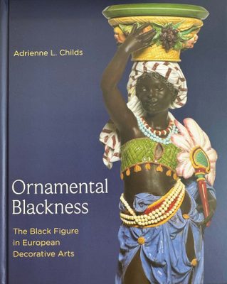 Cover of the book Ornamental Blackness by Adrienne L. Childs, featuring a photo of a colourfully painted sculpture of a black woman carrying a basket on her head supported by one arm, and a feathered fan in her left hand.