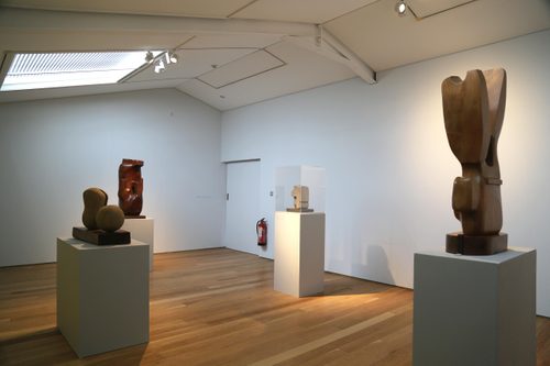 A gallery space with several small abstract sculptures carved from wood and stone, each displayed on a plinth.
