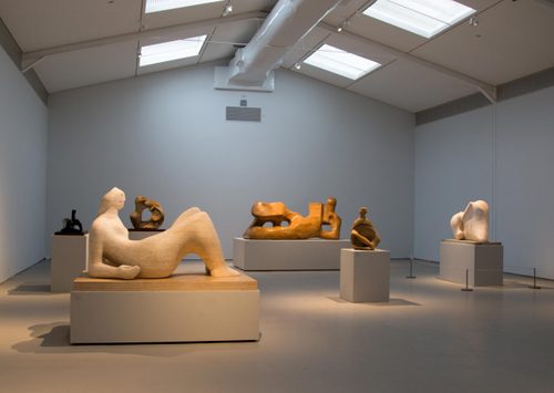 Wide shot of a large gallery space, filled with large figurative sculptures by Henry Moore, carved from wood and stone.
