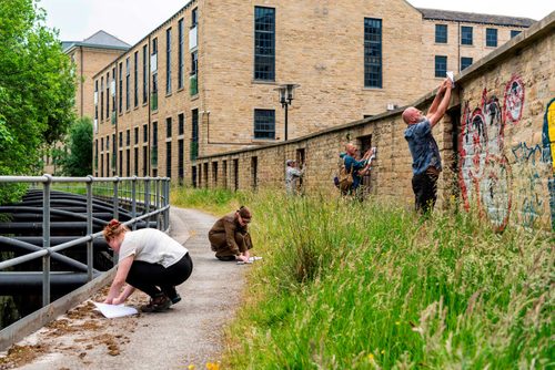 Six adults making rubbings on paper, using the textured surfaces of stone walls and the pavement alongside a canal.