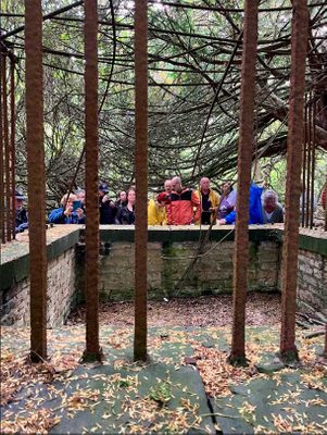 A group of people looking over a waist-high stone wall and metal gate at the supposed grave stone of Robin Hood.