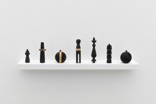 Seven small wooden objects, arranged in a line on a shelf. They have all been 'decorated' with different patterns of black lines, burnt by the sun using a magnifying glass.