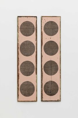 Two rectangular pieces of driftwood with chipped pale pink paint in the background and a sequence of four circles burnt vertically into the each piece of wood