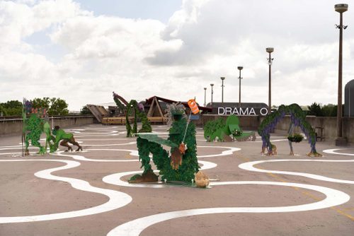 Five metal sculptures of human-plant hybrid characters, displayed on a concrete rooftop space.